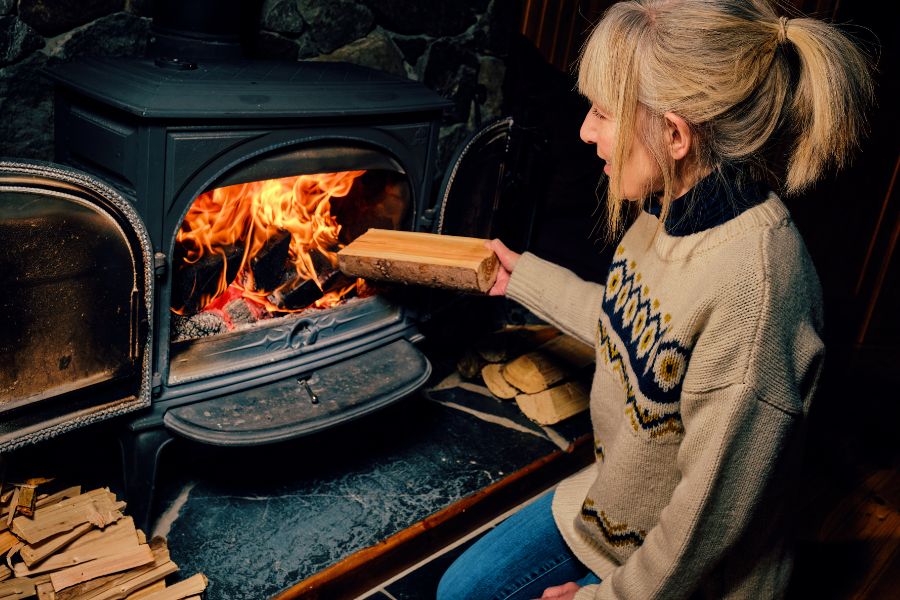 woman holding a log of wood in front of a wood burning stove